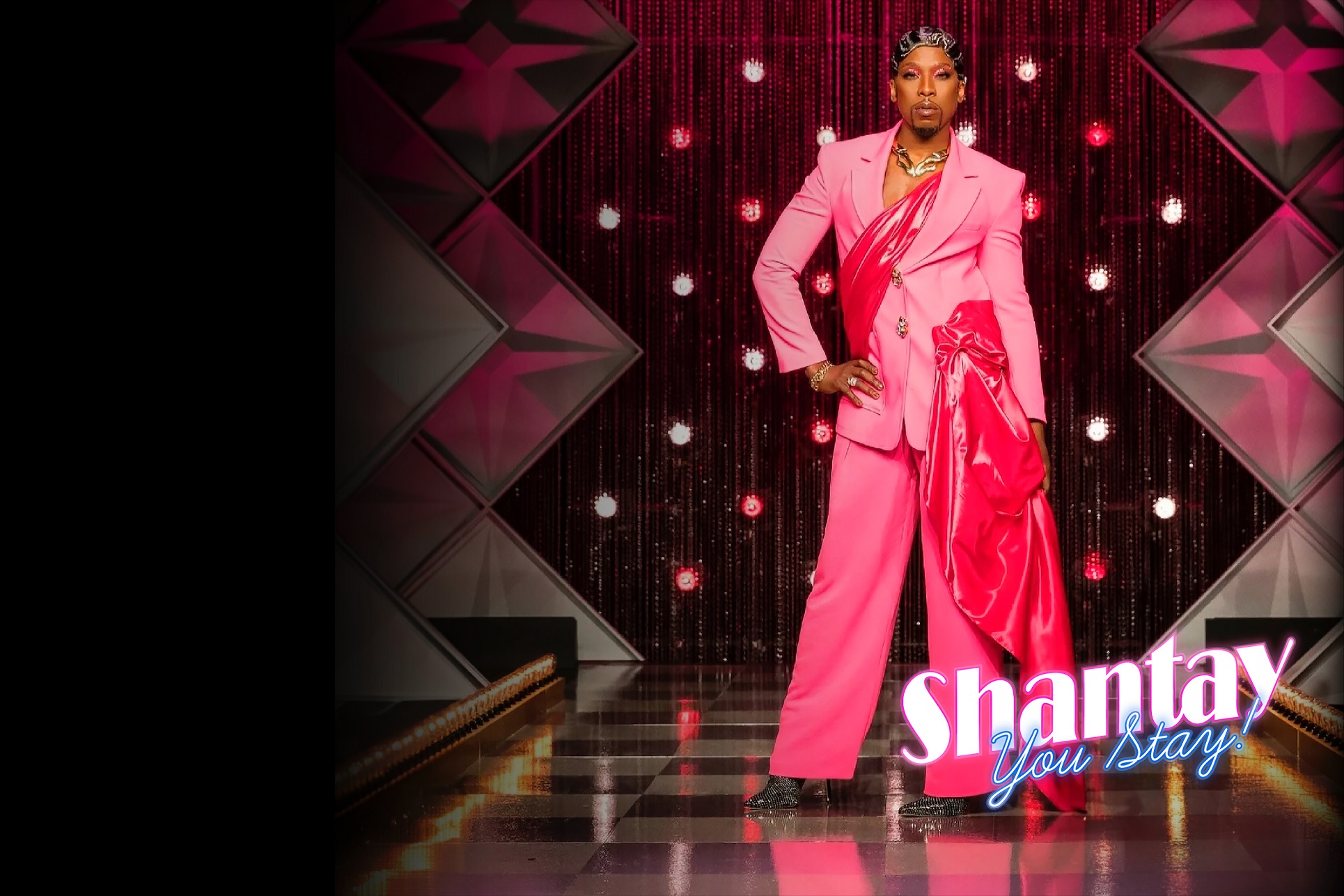 The image depicts a person in a vibrant pink suit standing confidently on a stage. The backdrop features star-shaped decorations and twinkling lights. The text “Shantay You Stay” is displayed at the bottom.